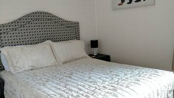 A neatly made bed with a patterned bedspread and pillows, a bedside table with a lamp, and a wall-mounted picture of a bear.