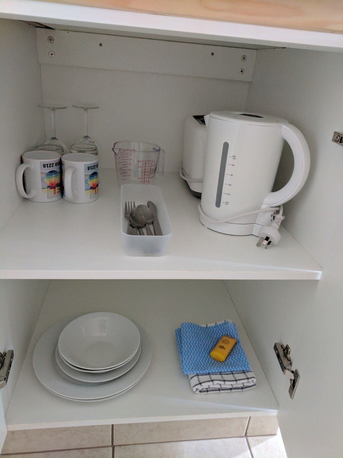 A kitchen with a kettle, measuring cups, and mugs on the countertop.