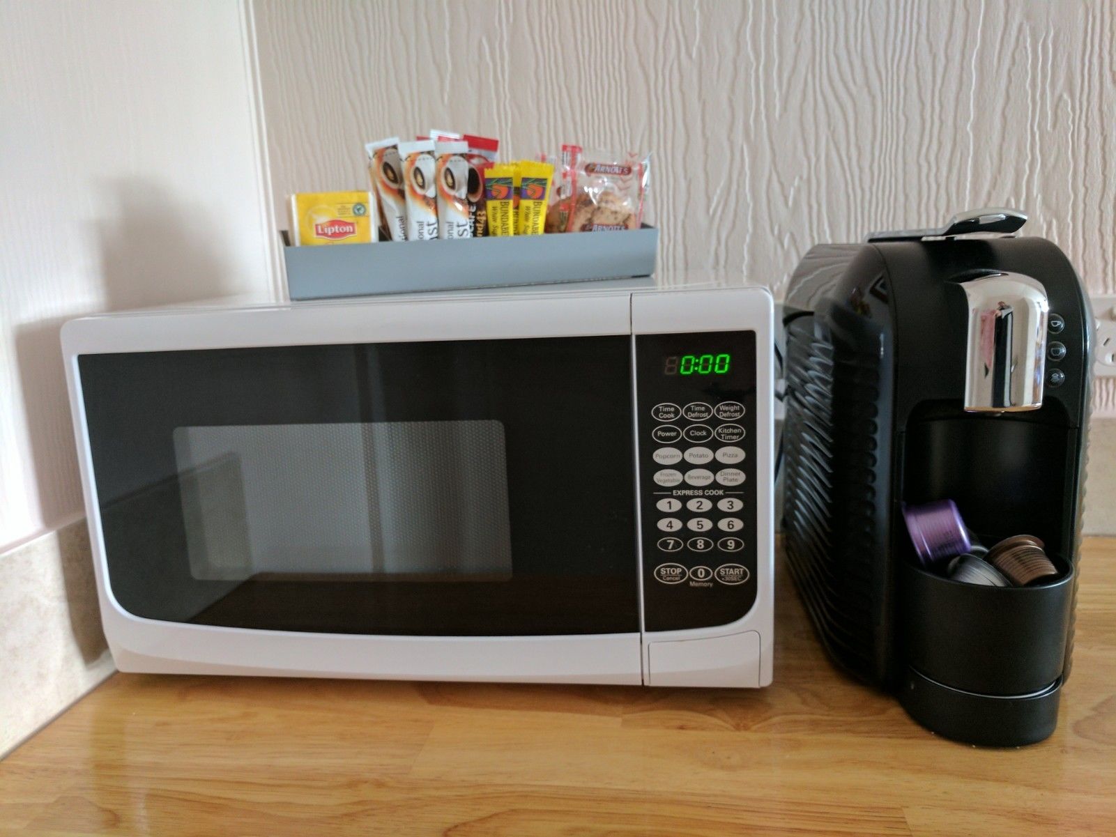 Un four à micro-ondes doté d’un écran numérique et d’un panneau de commande, posé sur un plan de travail en bois, à côté d’une machine à café.
