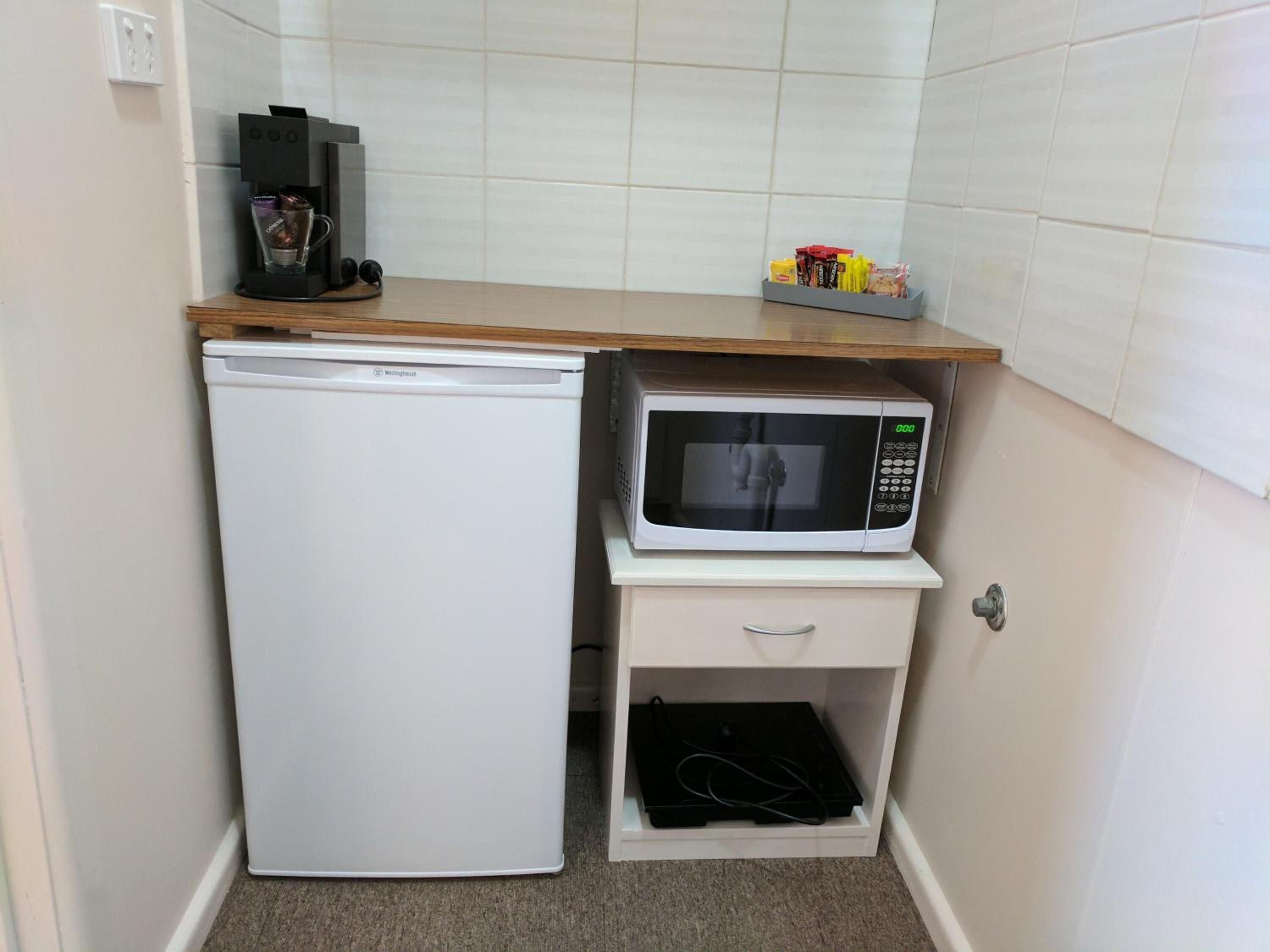 A compact kitchen with a white refrigerator, a microwave, and a coffee machine on a wooden countertop.