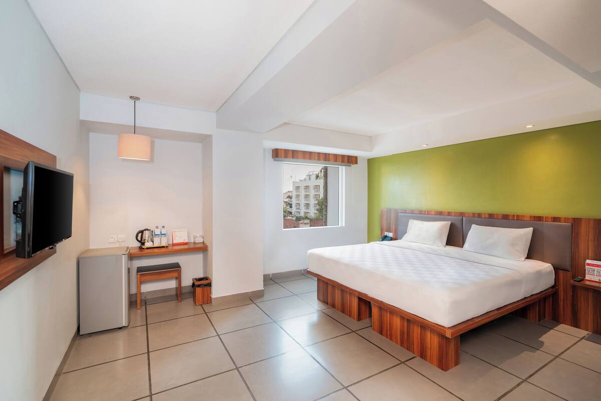 A modern hotel room with a bed, a desk, a television, and a window.