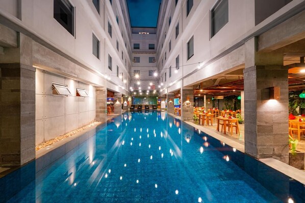 Een hotelinterieur met een centraal gelegen zwembad, verschillende eetgedeeltes en een modern architectonisch ontwerp.