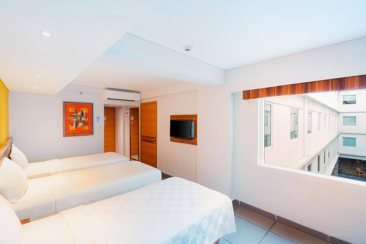 A hotel room with two beds, a TV mounted on the wall, and a window overlooking a building.