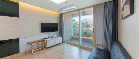 Una sala moderna con televisor de pantalla plana, un escritorio de madera, un sofá acolchado y un balcón con vistas al exterior.