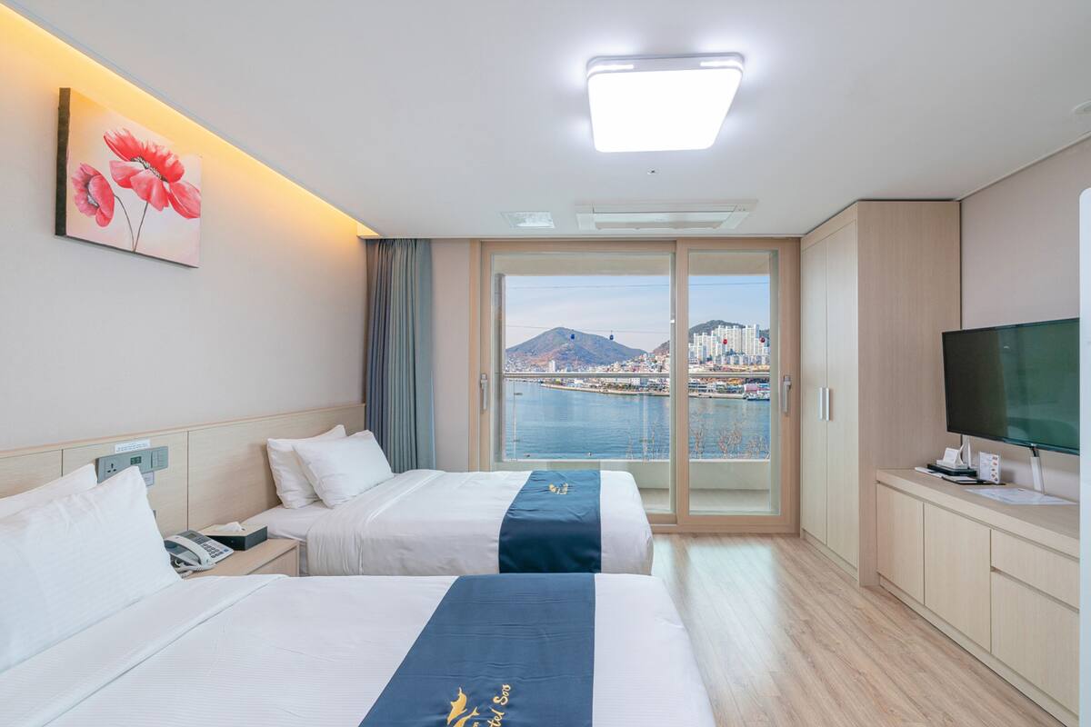 A hotel room with two beds, a TV, and a view of a cityscape and water.