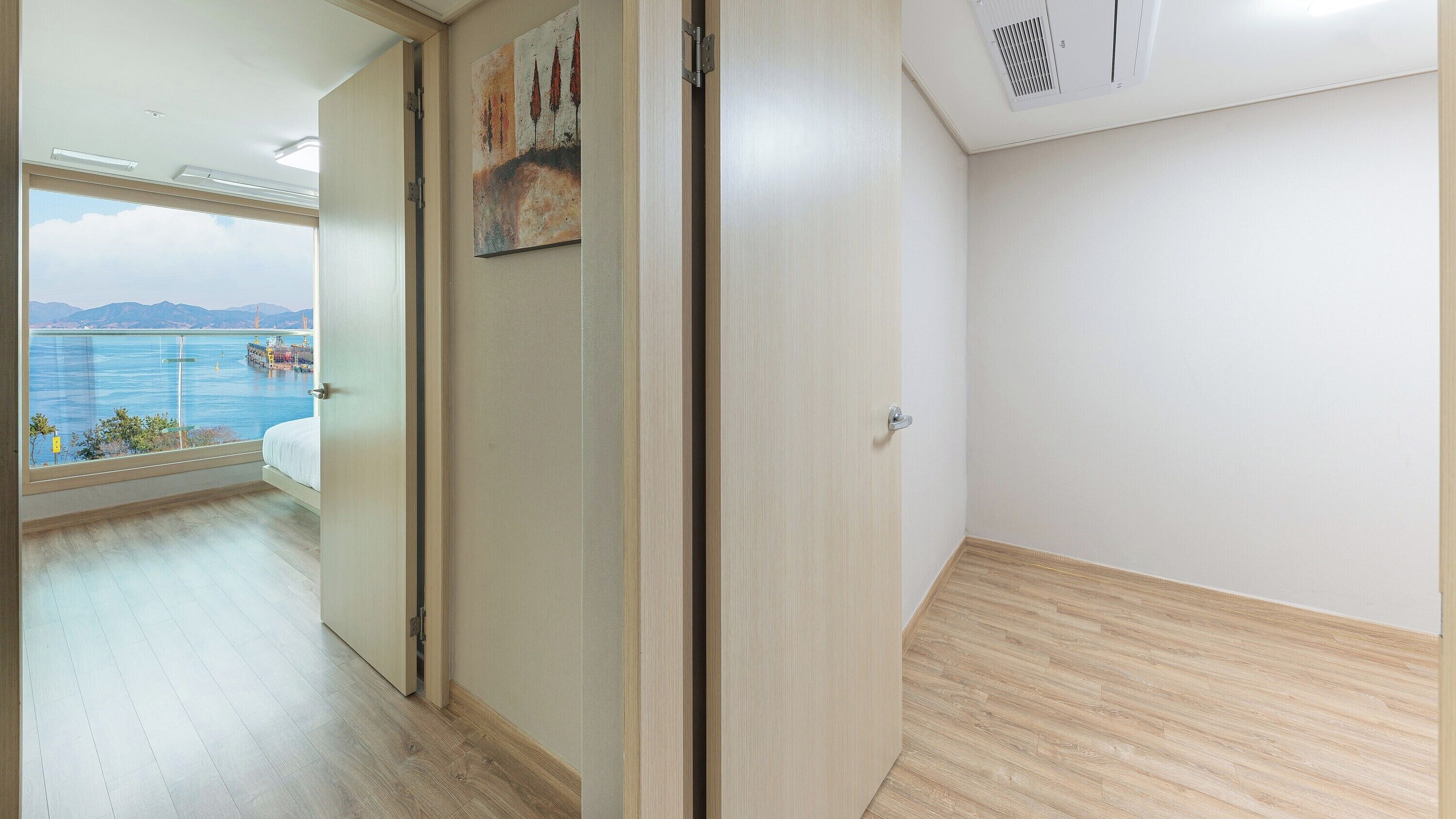 Habitación de hotel con un amplio ventanal que ofrece vista a un cuerpo de agua y montañas distantes.