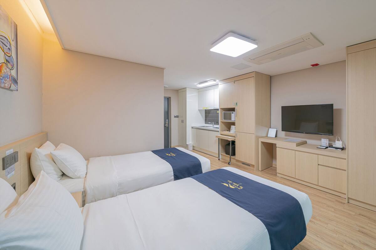 A hotel room with two beds, a kitchenette, a TV, and a wardrobe.