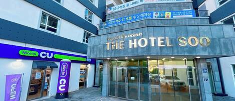 Entrada de un hotel con un letrero que dice "The Hotel Soo" y un cartel que dice "Nice to CU" cerca.