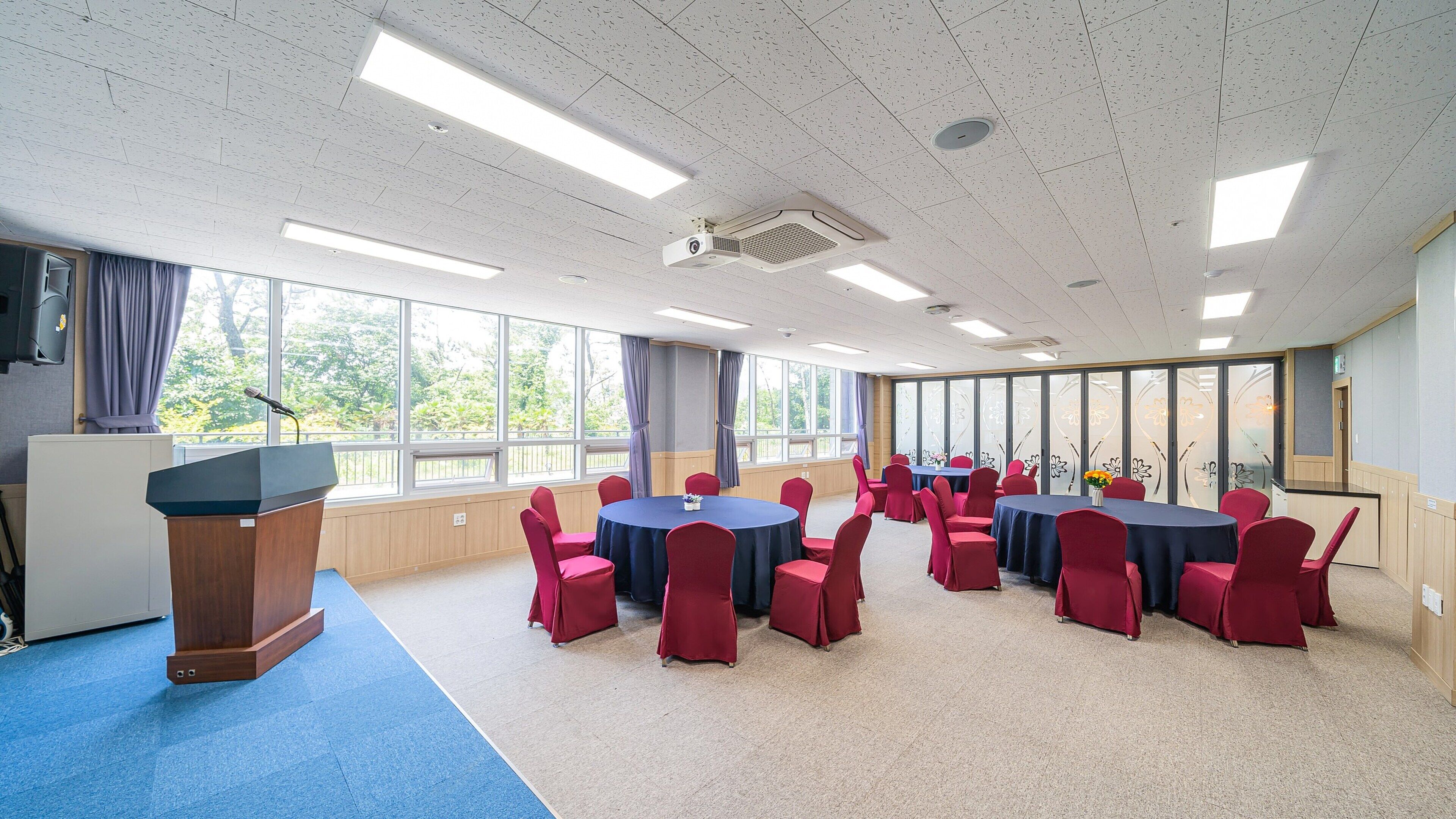 Une salle de conférence équipée d’un pupitre, de tables rondes et de chaises rouges.