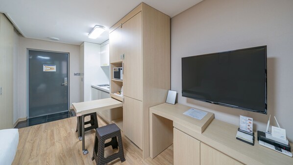 Une chambre d’hôtel compacte dotée d’une kitchenette, d’un grand téléviseur à écran plat, d’un bureau avec une chaise et d’un petit tabouret.