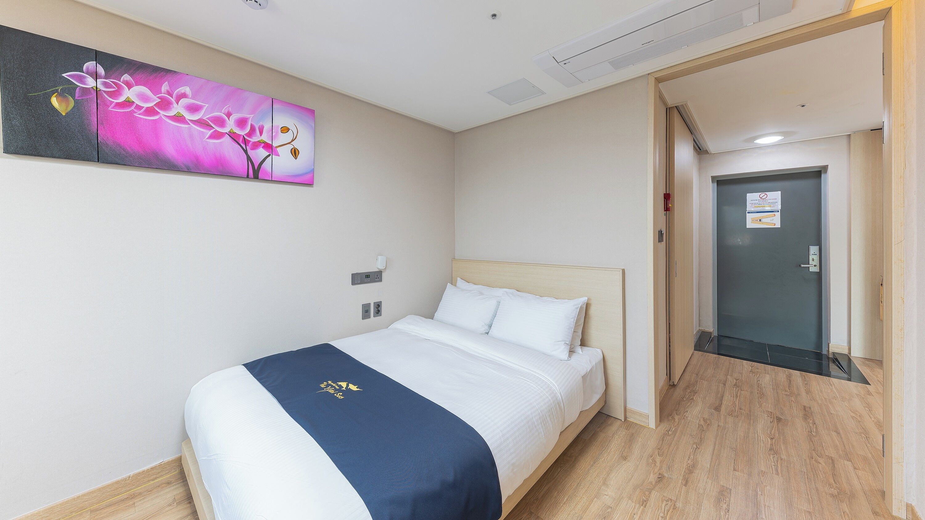A hotel room with a bed, a painting on the wall, and a door to the right.