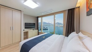 A hotel room with a bed, a TV, a desk, and a view of a body of water. - The Hotel Soo (Yeosu)