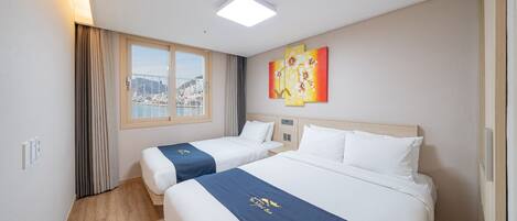 A hotel room with two beds, a city view, a painting on the wall, and a ceiling light.