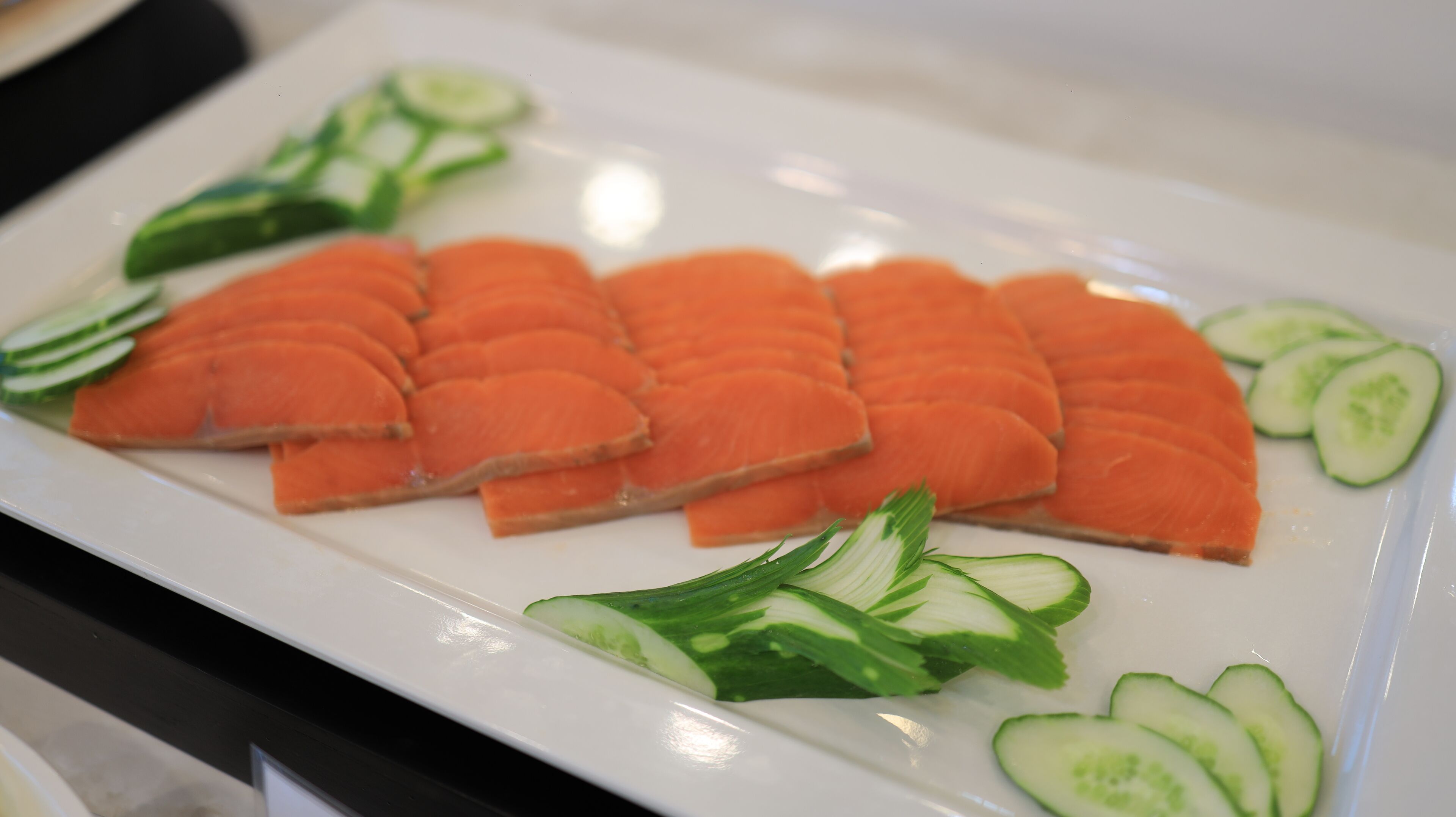 A white plate with neatly arranged slices of salmon and cucumber slices.