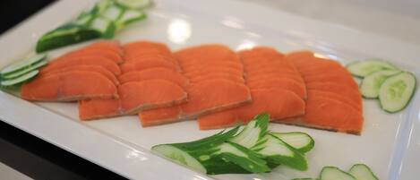 A white plate with neatly arranged slices of salmon and cucumber slices.