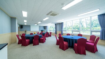 Un salón de conferencias con mesas redondas, sillas rojas y ventanas amplias.