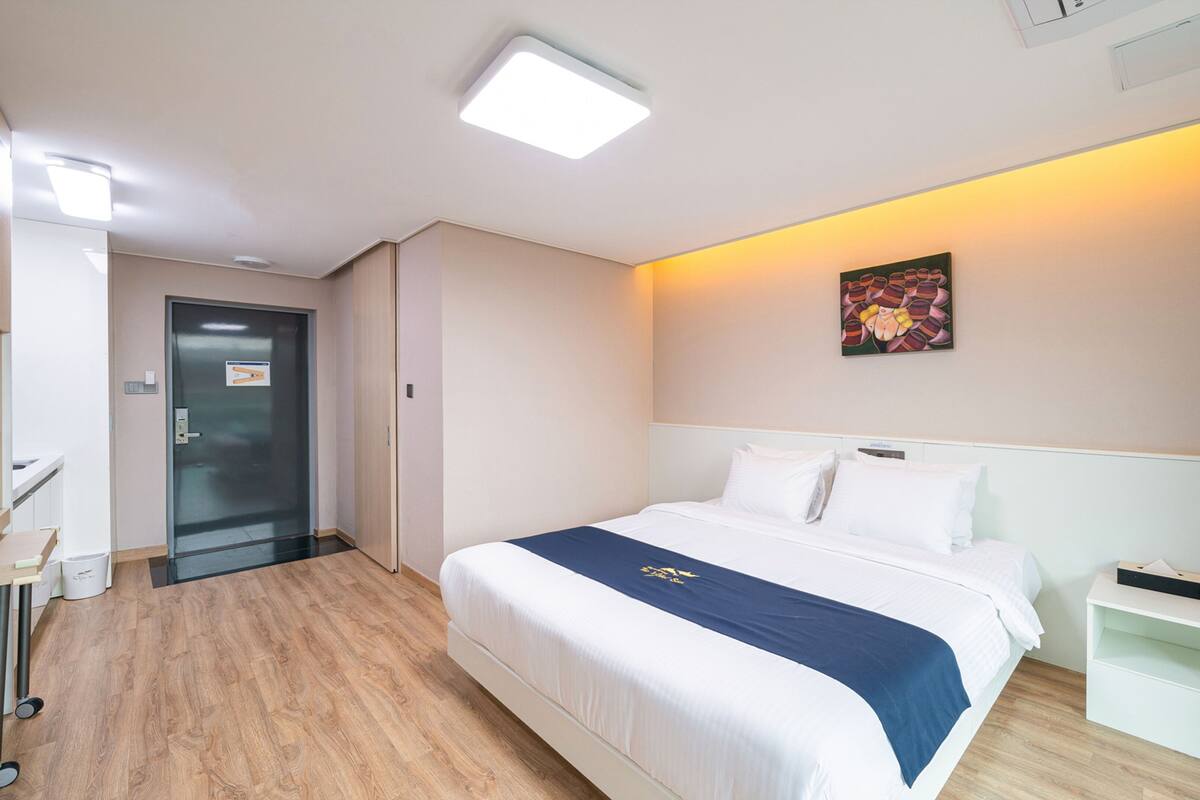 A hotel room with a bed, bedside table, and a small desk with a chair.