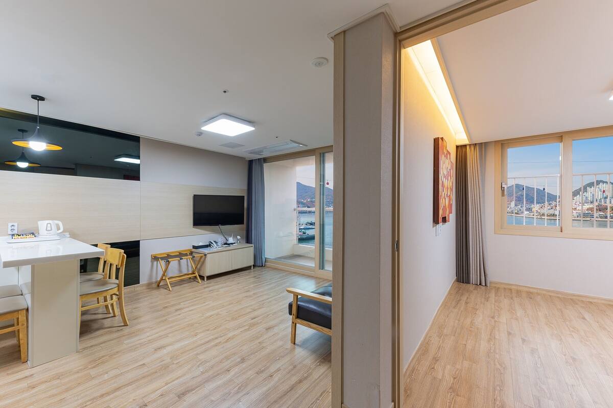 A modern kitchen with a dining area, a flat-screen TV, and a view of a cityscape through large windows.