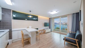 A modern kitchen with a dining area, a sofa, and a large window with a view of a body of water and mountains. - The Hotel Soo (Yeosu)