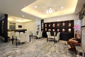 A modern hotel lobby with marble flooring, white chairs, a reception desk, and a wall of decorative stone sculptures.