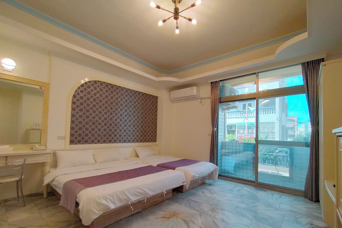 A hotel room with two beds, a desk, a chair, a large window, and a ceiling light fixture.