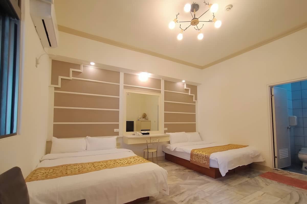 A hotel room with two beds, a desk, a mirror, and a bathroom visible through an open door.