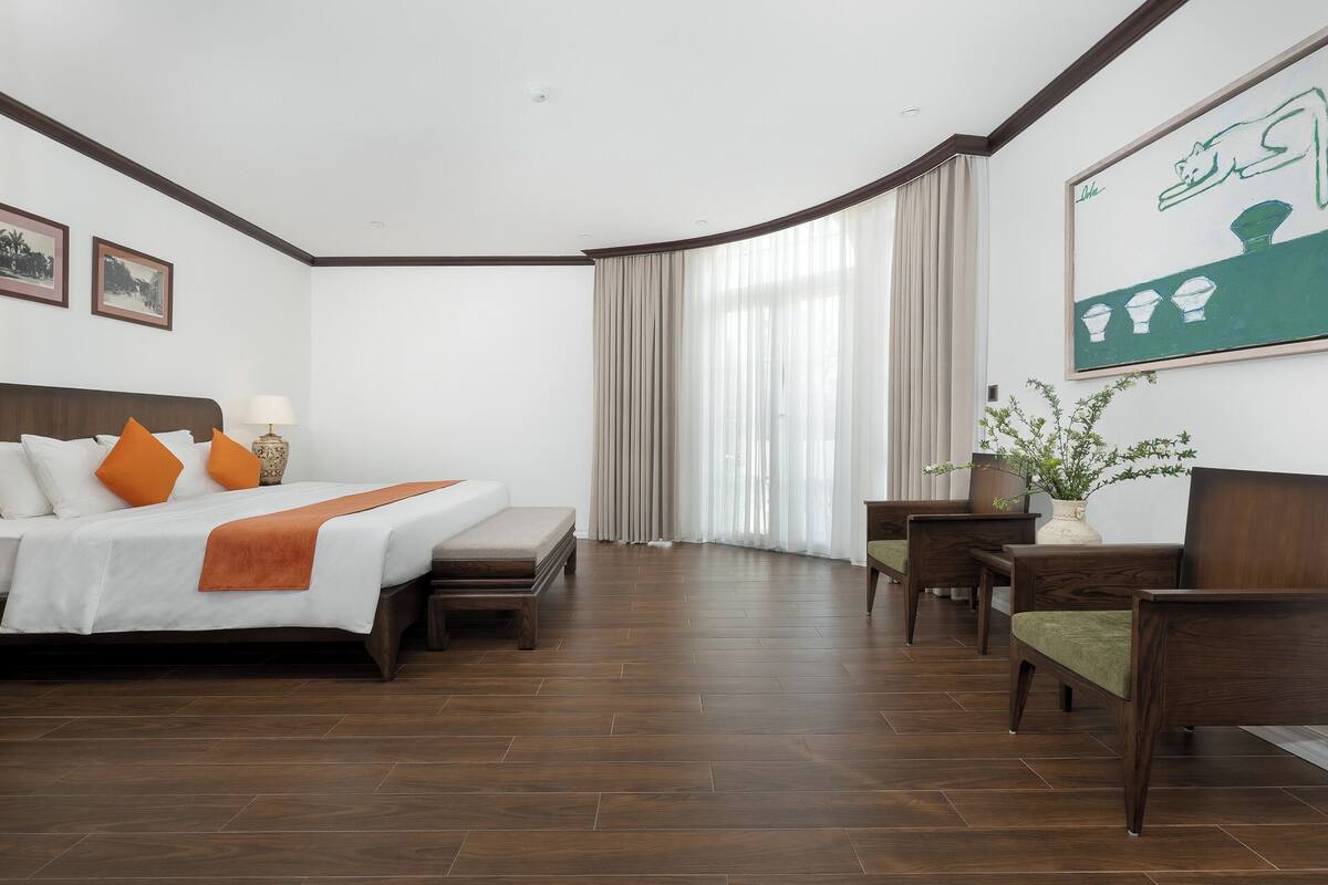 Habitación de hotel con cama, escritorio, silla, ventana con cortinas y un cuadro en la pared.