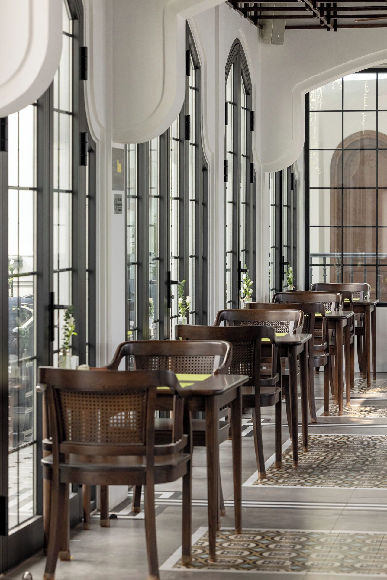 A modern interior with high windows, wooden furniture, and patterned flooring.