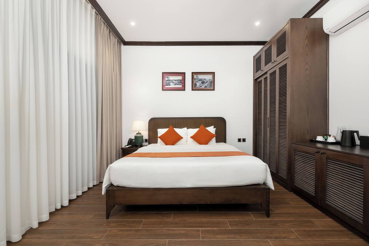 Habitación de hotel con cama, mesita de noche, lámpara, armario y dos cuadros en la pared.