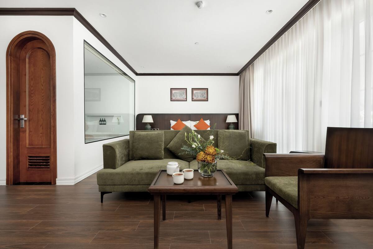 Habitación de hotel moderna con un sofá verde, una mesa de centro de madera y vista a la ciudad por la ventana.