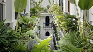 Un amplio atrio con una escalera central, rodeado de exuberante vegetación tropical y columnas arquitectónicas blancas.