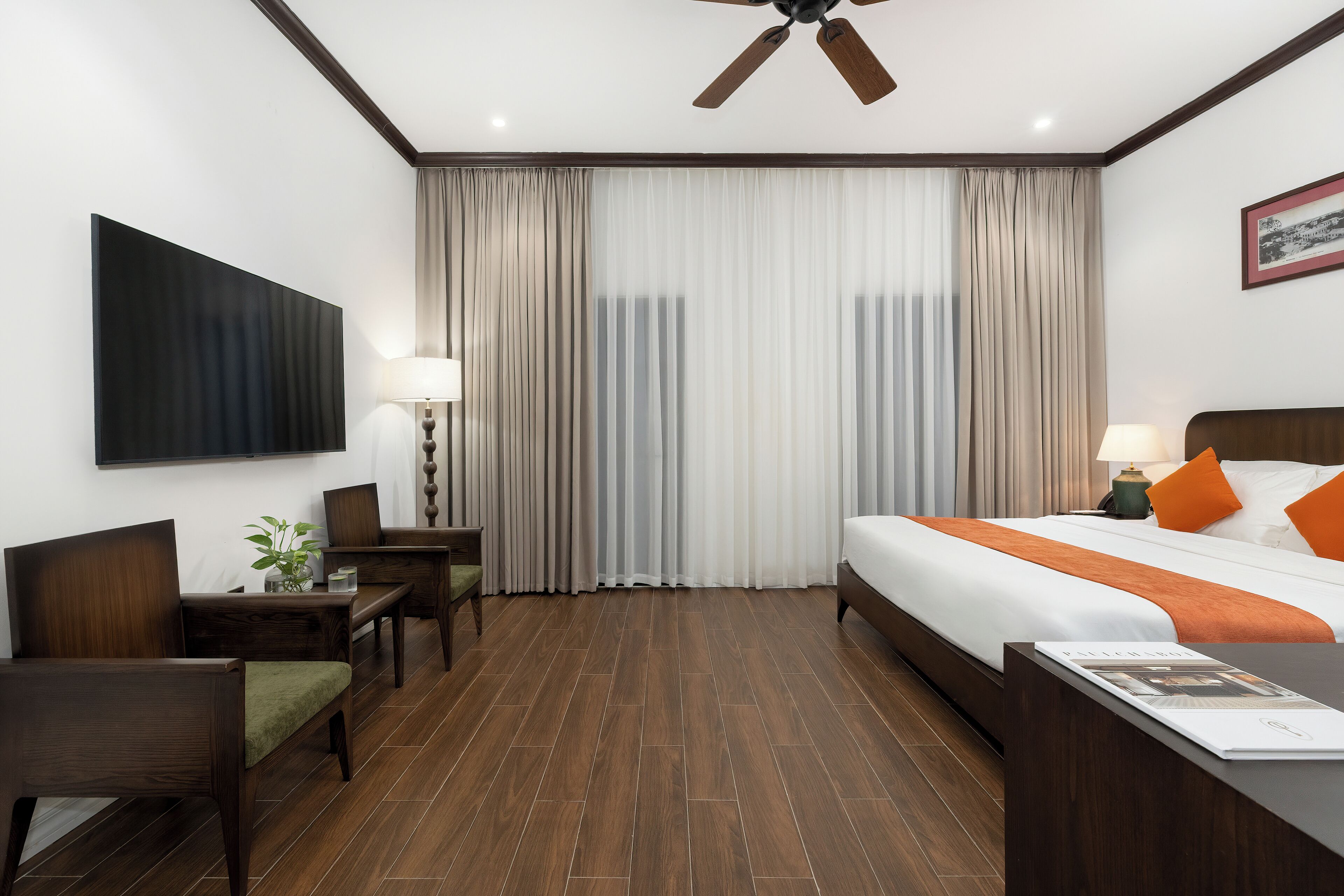 Quarto de hotel com cama, escrivaninha, cadeira e uma televisão grande na parede.