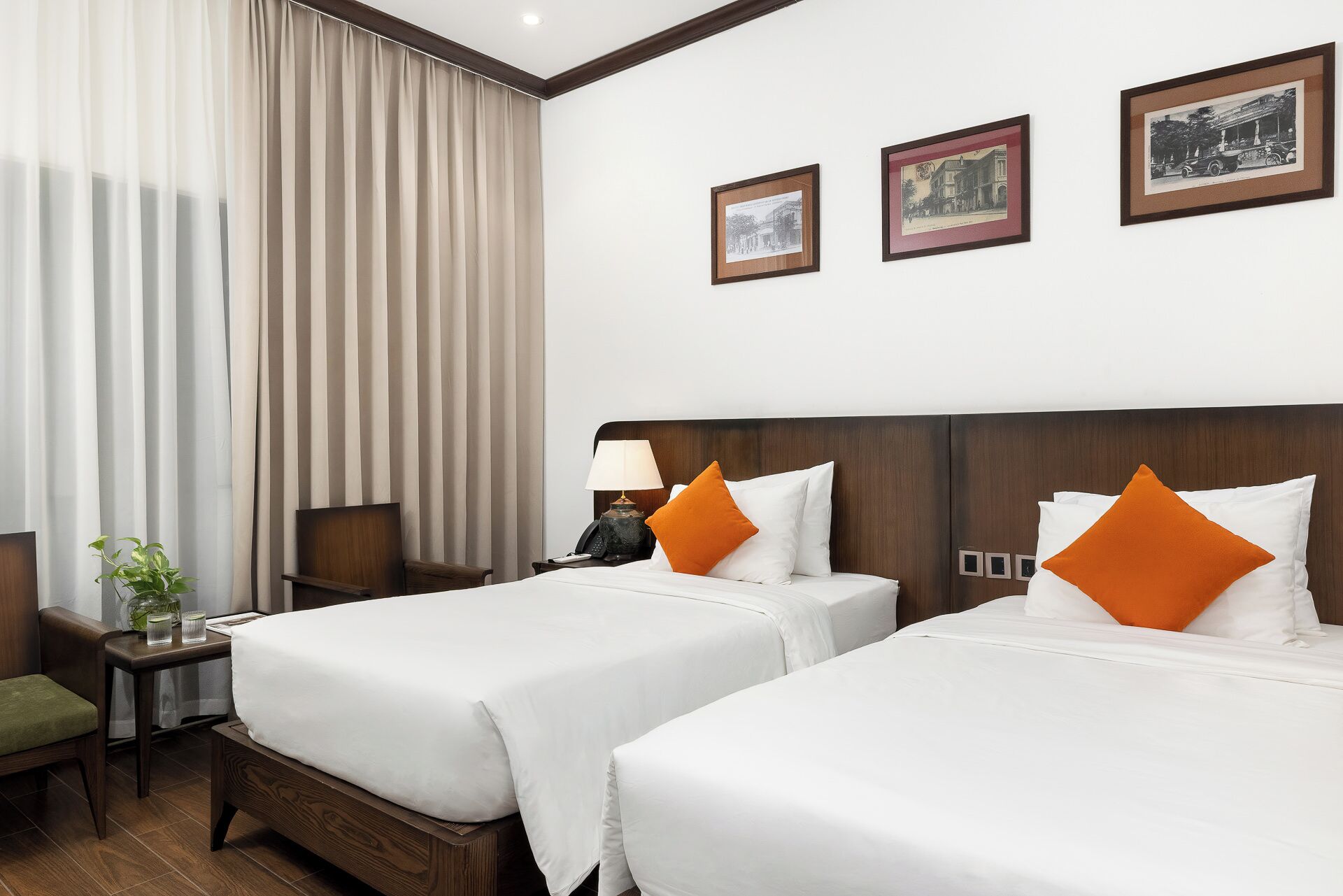 A hotel room with two beds, a nightstand, a lamp, a chair, and a plant.