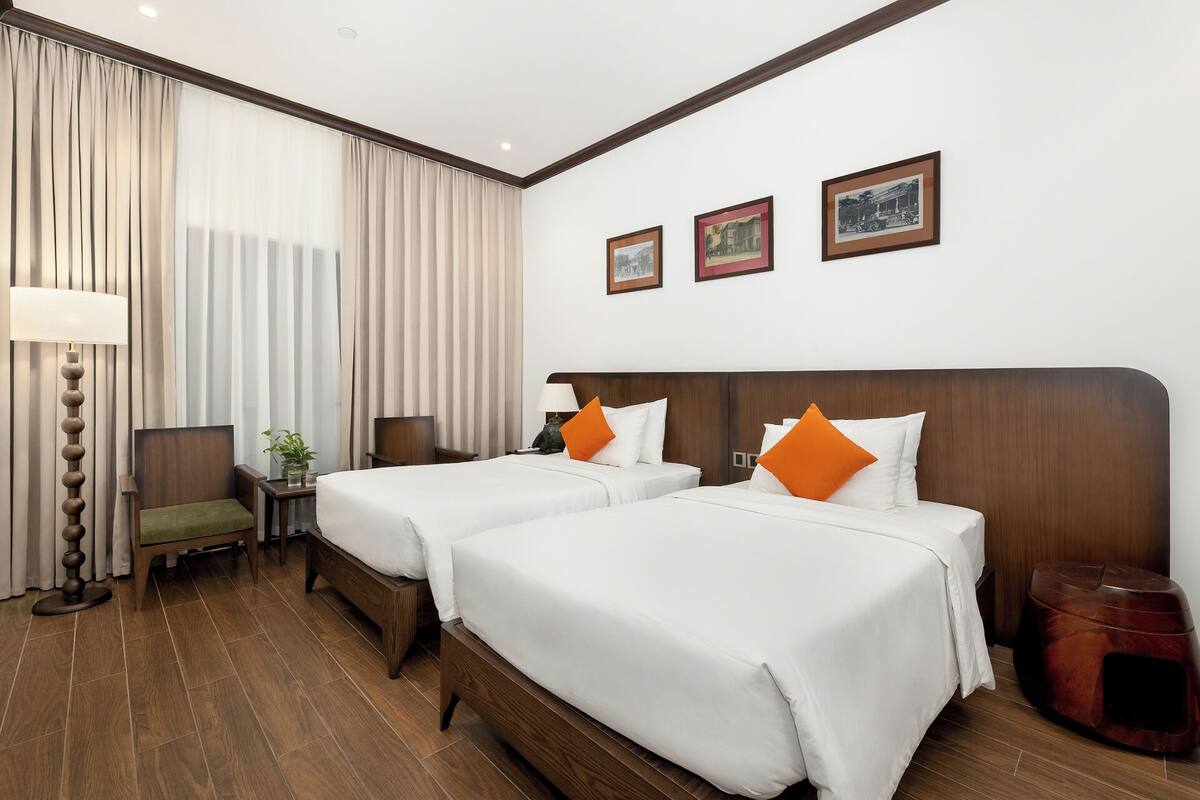 Una habitación de hotel con dos camas, una silla, una lámpara y una mesita.