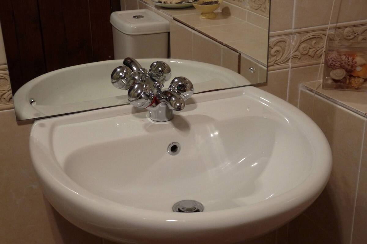 Un lavamanos blanco con espejo arriba, un inodoro a la izquierda y una pared con azulejos y un borde decorativo.