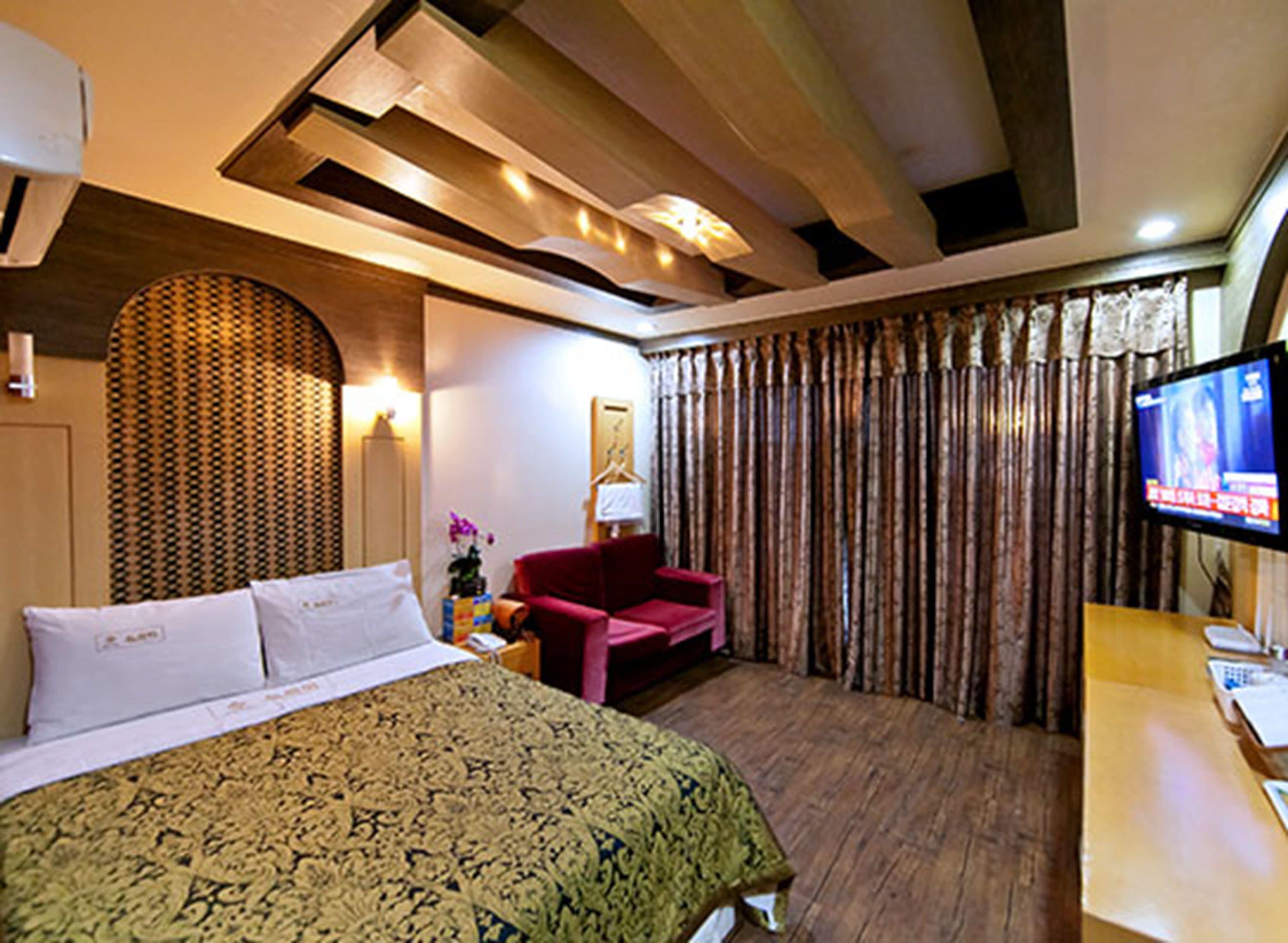 A hotel room with a large bed, a red armchair, a television, and a curtain.