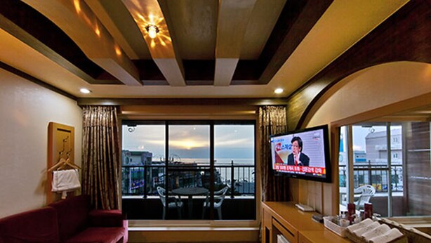 A hotel room with a large window, a television, a sofa, and a small kitchenette. - Drama Motel (Boryeong)