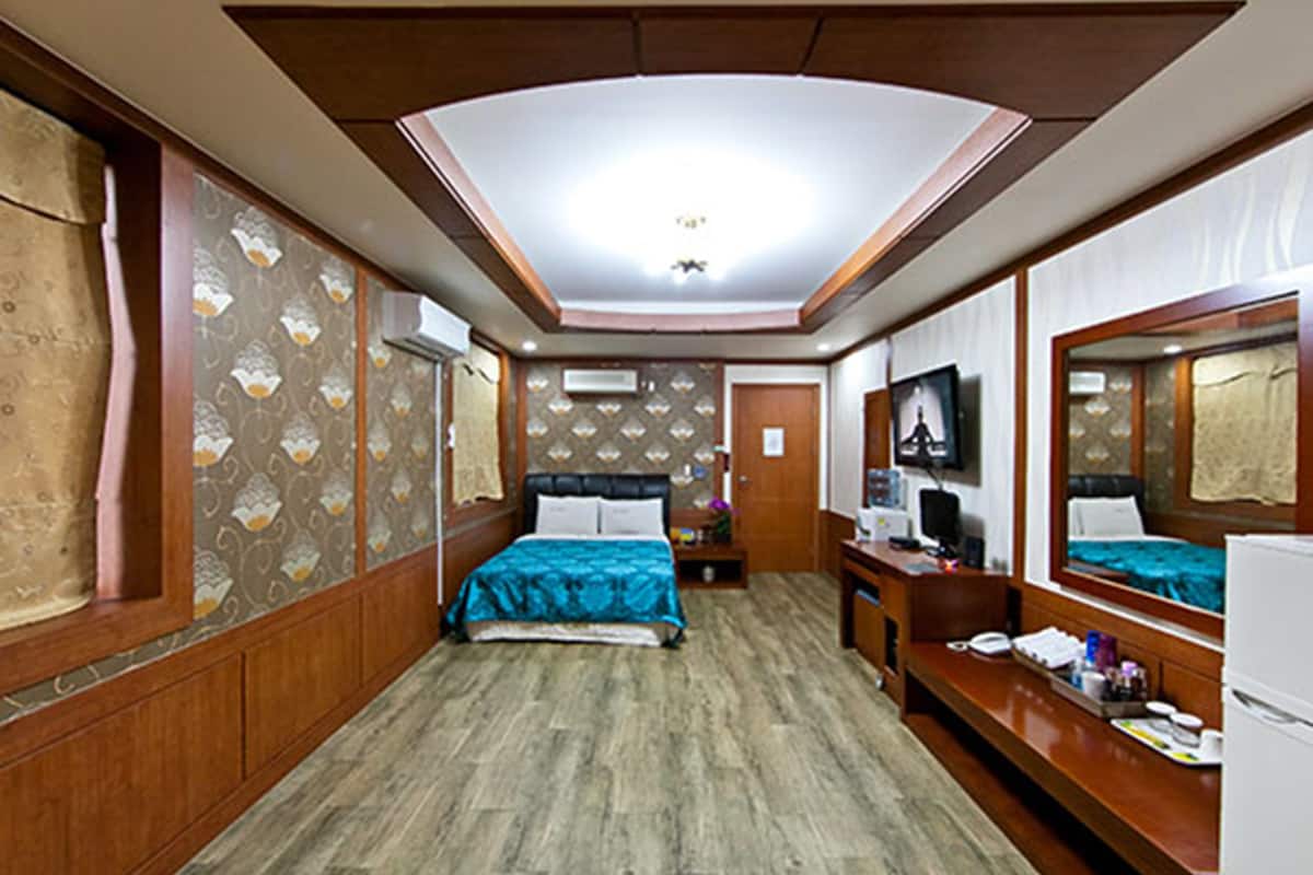 Una habitación de hotel funcional con cama, escritorio, silla, espejo y armario.