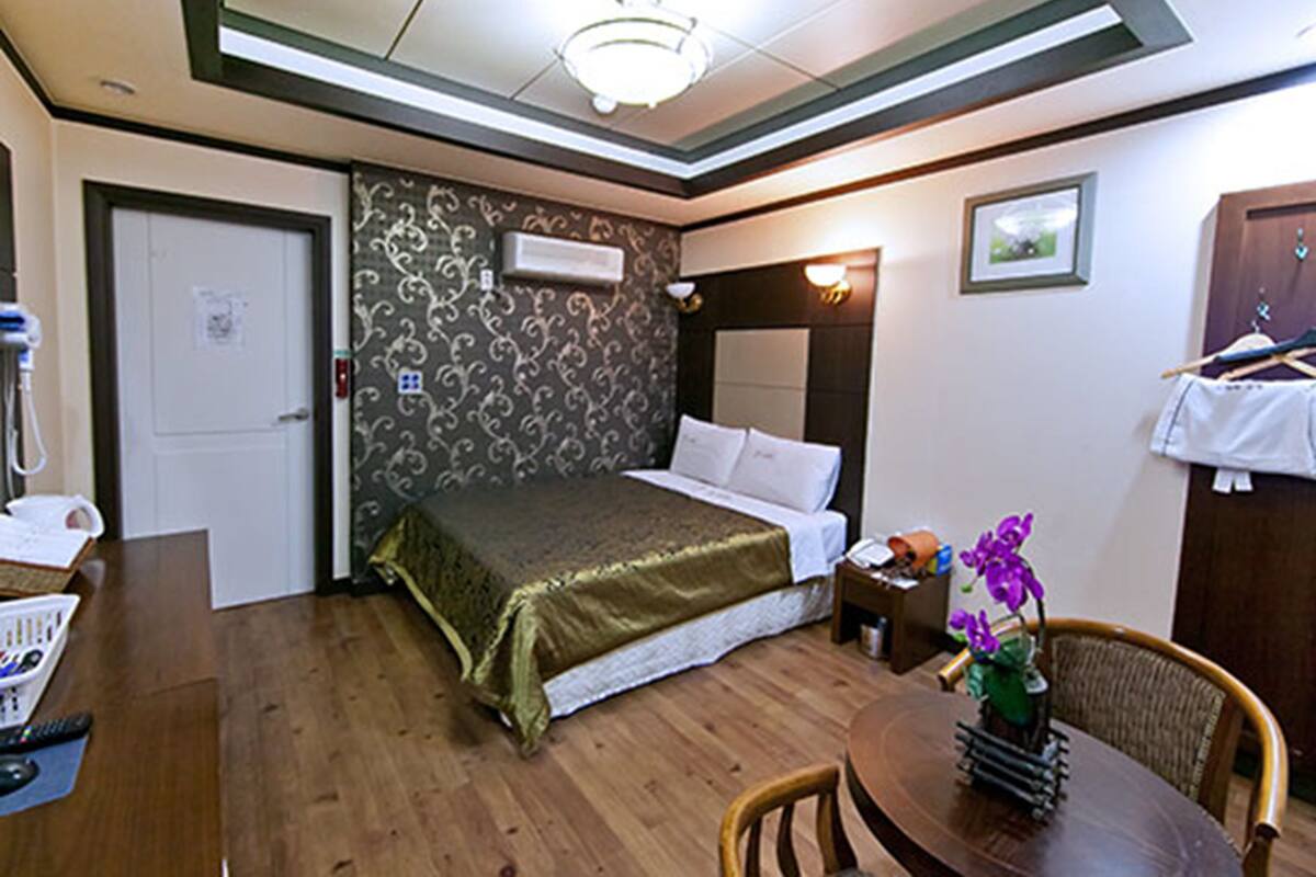 Una habitación de hotel con una cama, una mesita de noche y una pequeña mesa con un florero.
