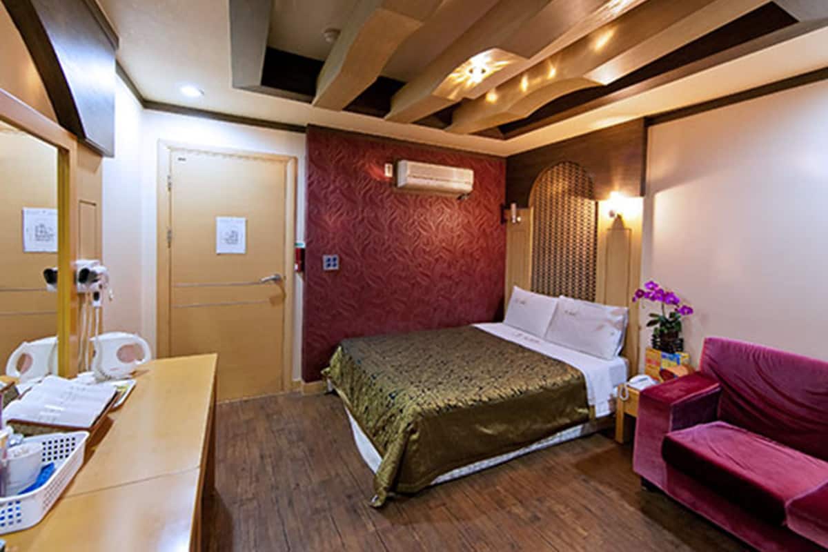 Una habitación de hotel con una cama, un escritorio con teléfono, un sofá rosa y un aire acondicionado instalado en la pared.
