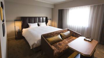 A hotel room with a large bed, a sofa, a small table, and a nightstand with a lamp.