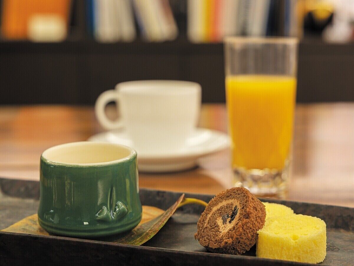 Bandeja de desayuno con una taza verde, una rebanada de pastel y un vaso de jugo de naranja.