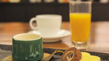 Bandeja de desayuno con una taza verde, una rebanada de pastel y un vaso de jugo de naranja.