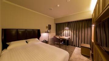 A hotel room with a large bed, a desk, a chair, a lamp, and a wardrobe.