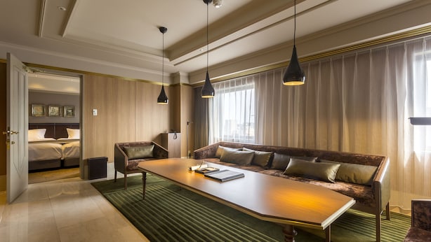 A hotel room with a large bed, a sofa, a dining table, and a view of the city through the window. - Royal Park Hotel Takamatsu (Takamatsu)