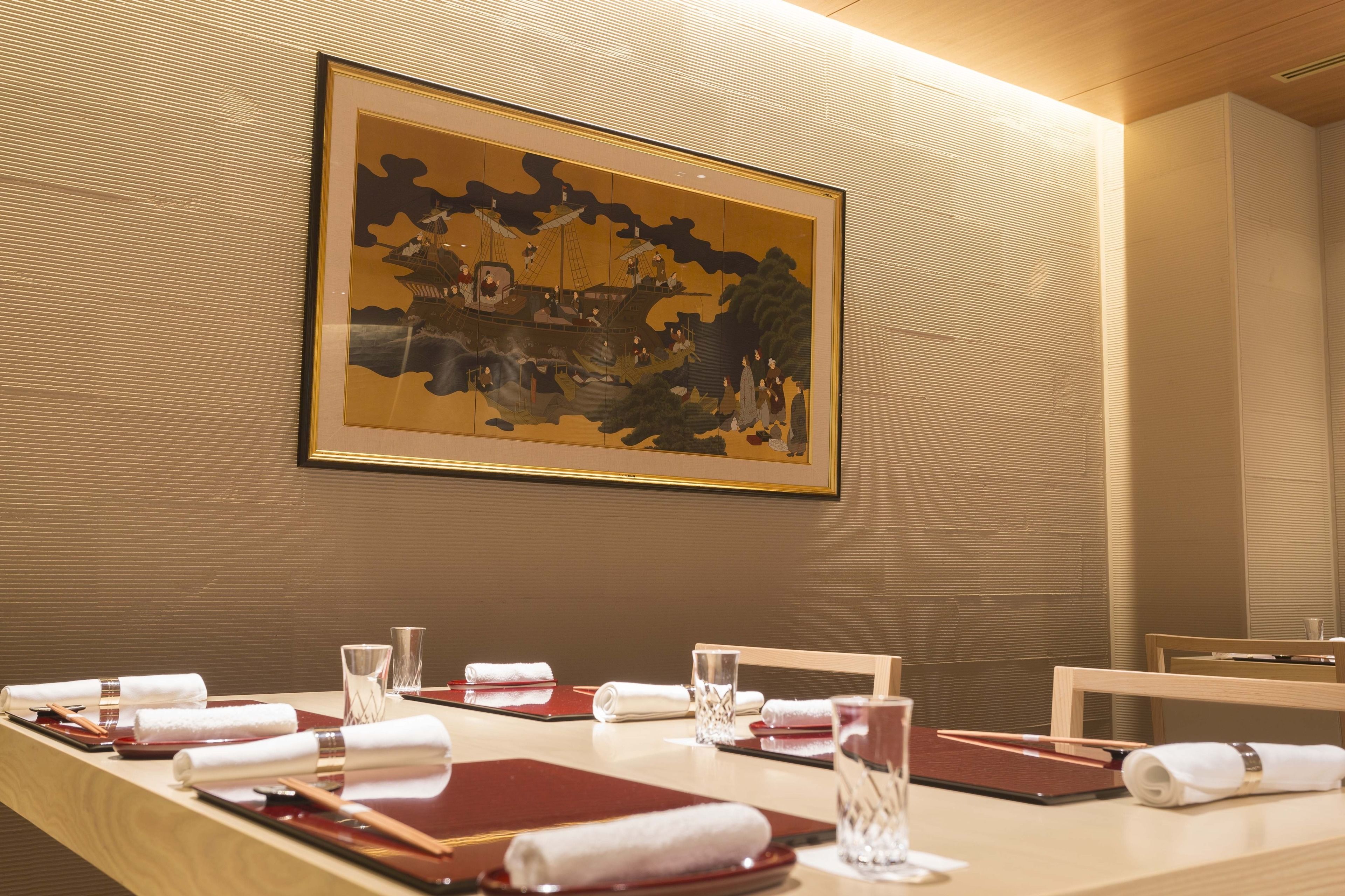 Una mesa de comedor elegantemente dispuesta con una obra de arte enmarcada encima, pared de madera y un interior moderno y limpio.