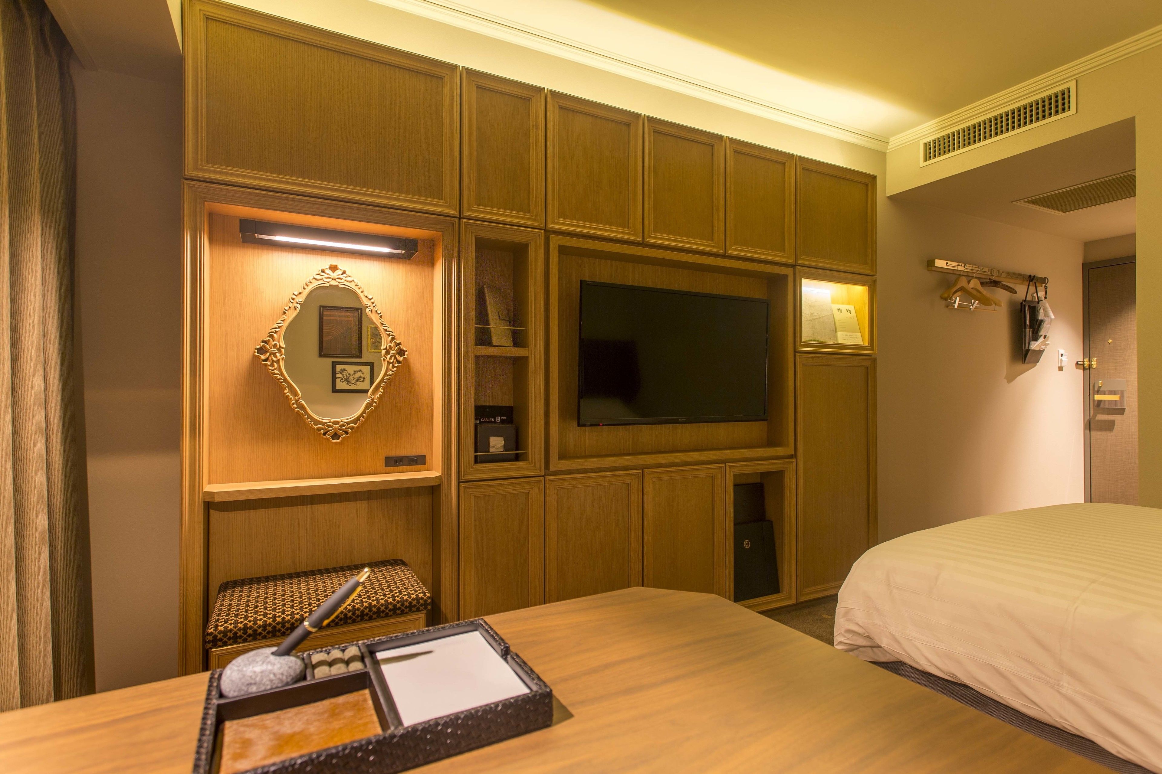 Una habitació d'hotel amb un llit gran, una televisió penjada a la paret, un armari de fusta amb mirall i una taula petita amb safata.