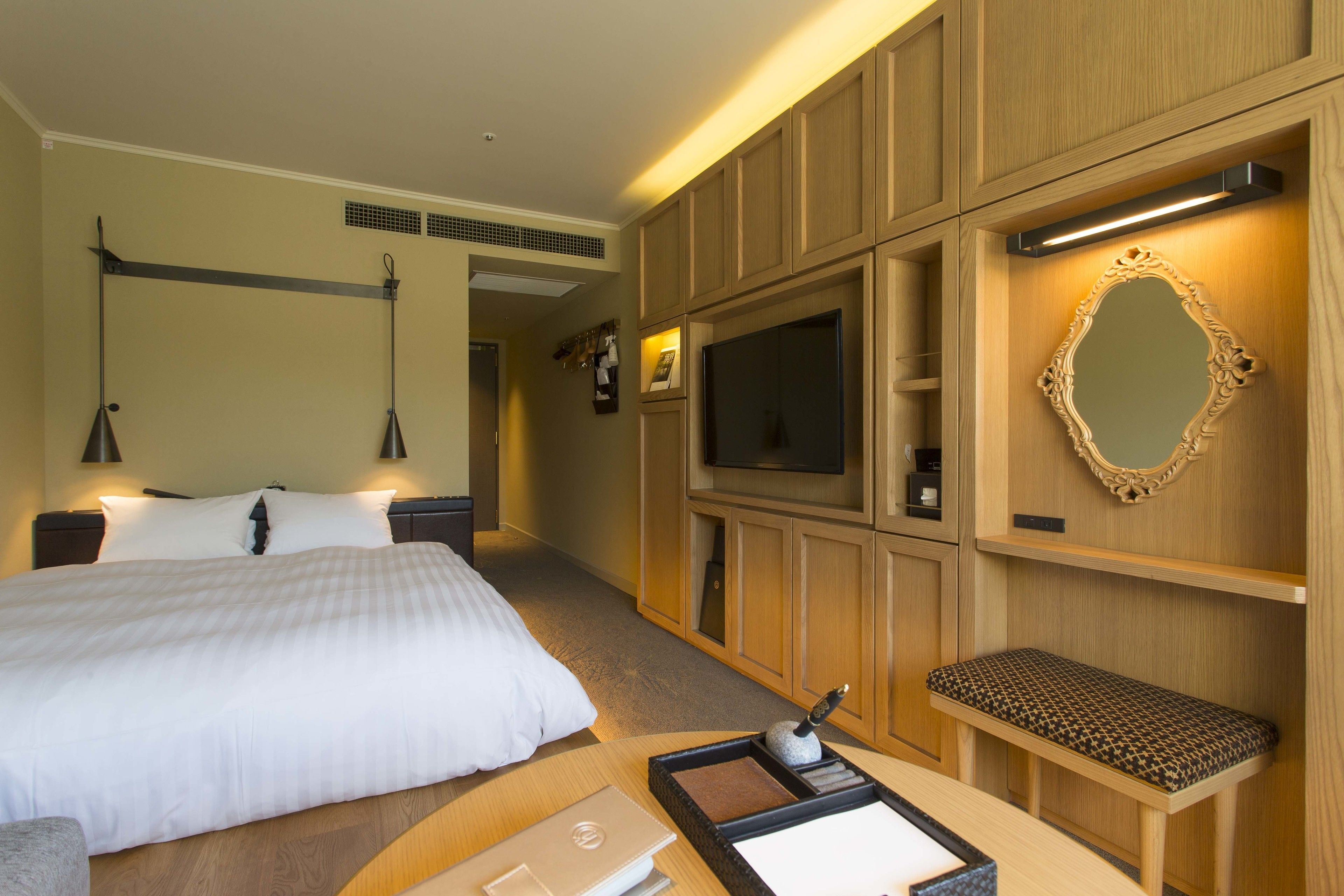 Una habitación de hotel con una cama grande, televisión, banco de madera y espejo.