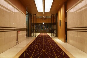 Un pasillo con alfombra de diseño geométrico, paredes de mármol e iluminación empotrada en el techo.