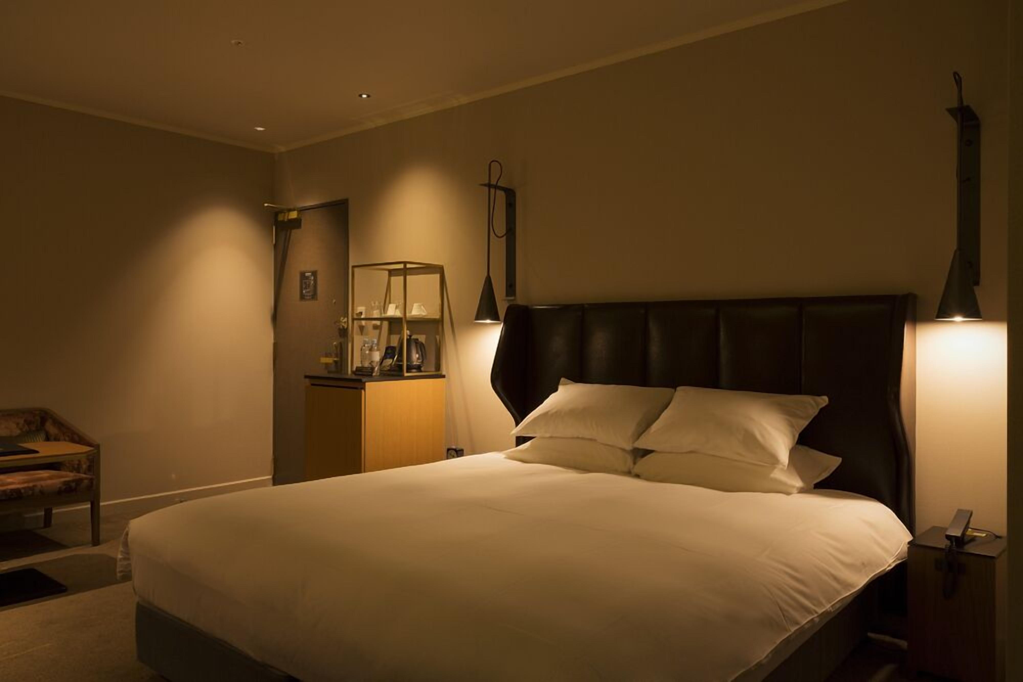 A neatly made bed with a dark headboard, a bedside table with a lamp, and a small cabinet with a mirror and decorative items.